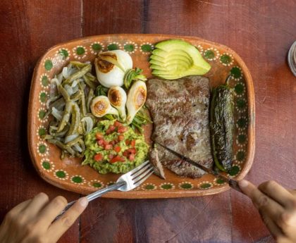 Authentic Mexican meal featuring grilled steak, avocado, and vegetables on a ceramic plate.